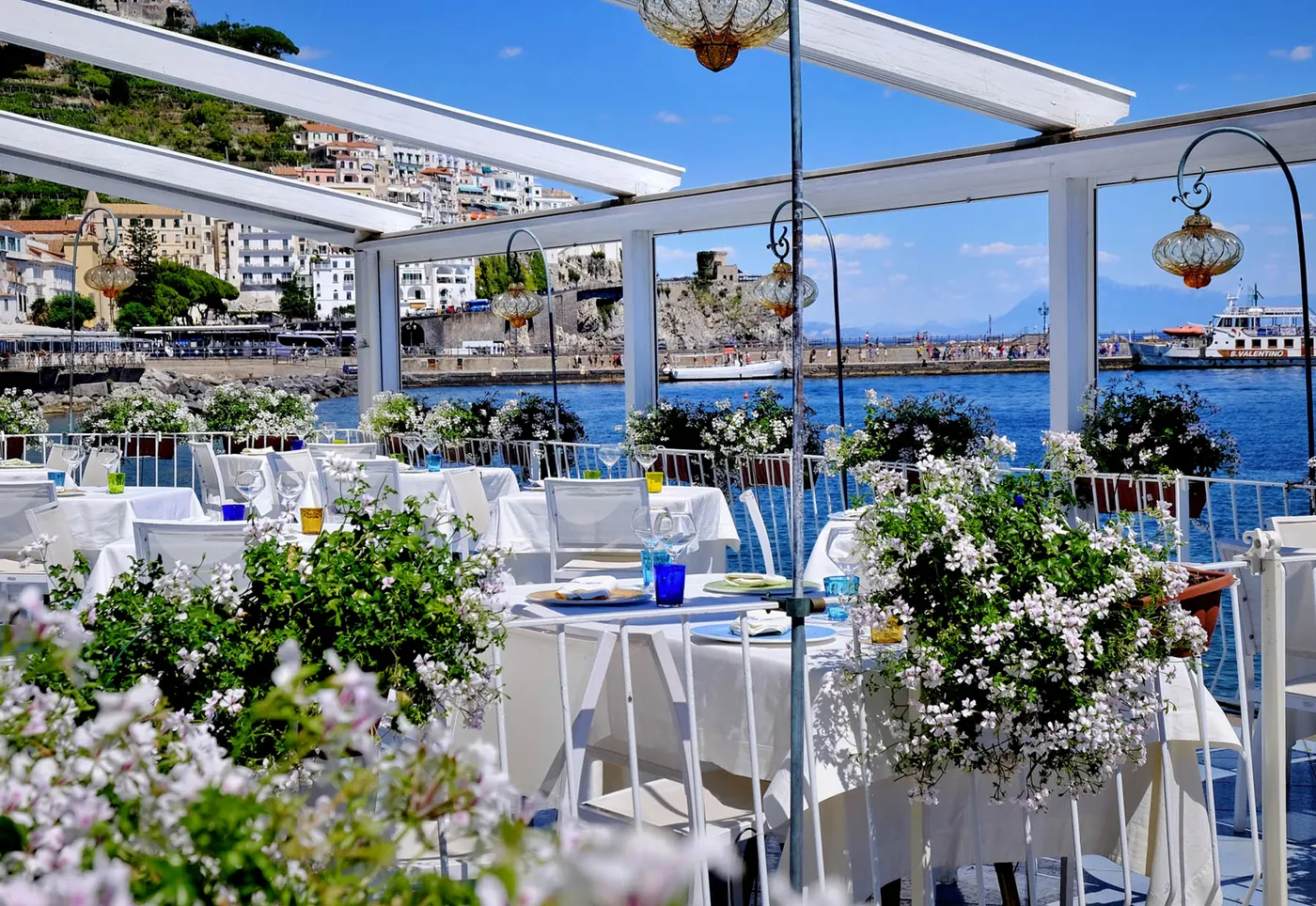 Tavoli apparecchiati sulla terrazza, tra fiori bianchi e vista sul mare